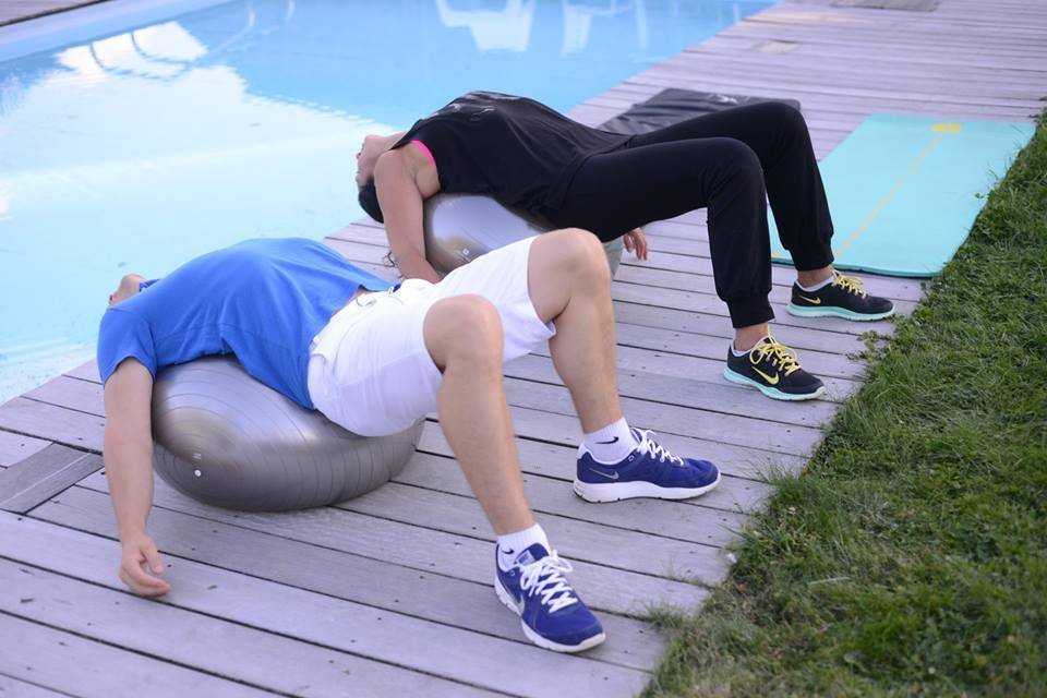 Coach et Cliente en exterieur pratique étirement sur swiss ball